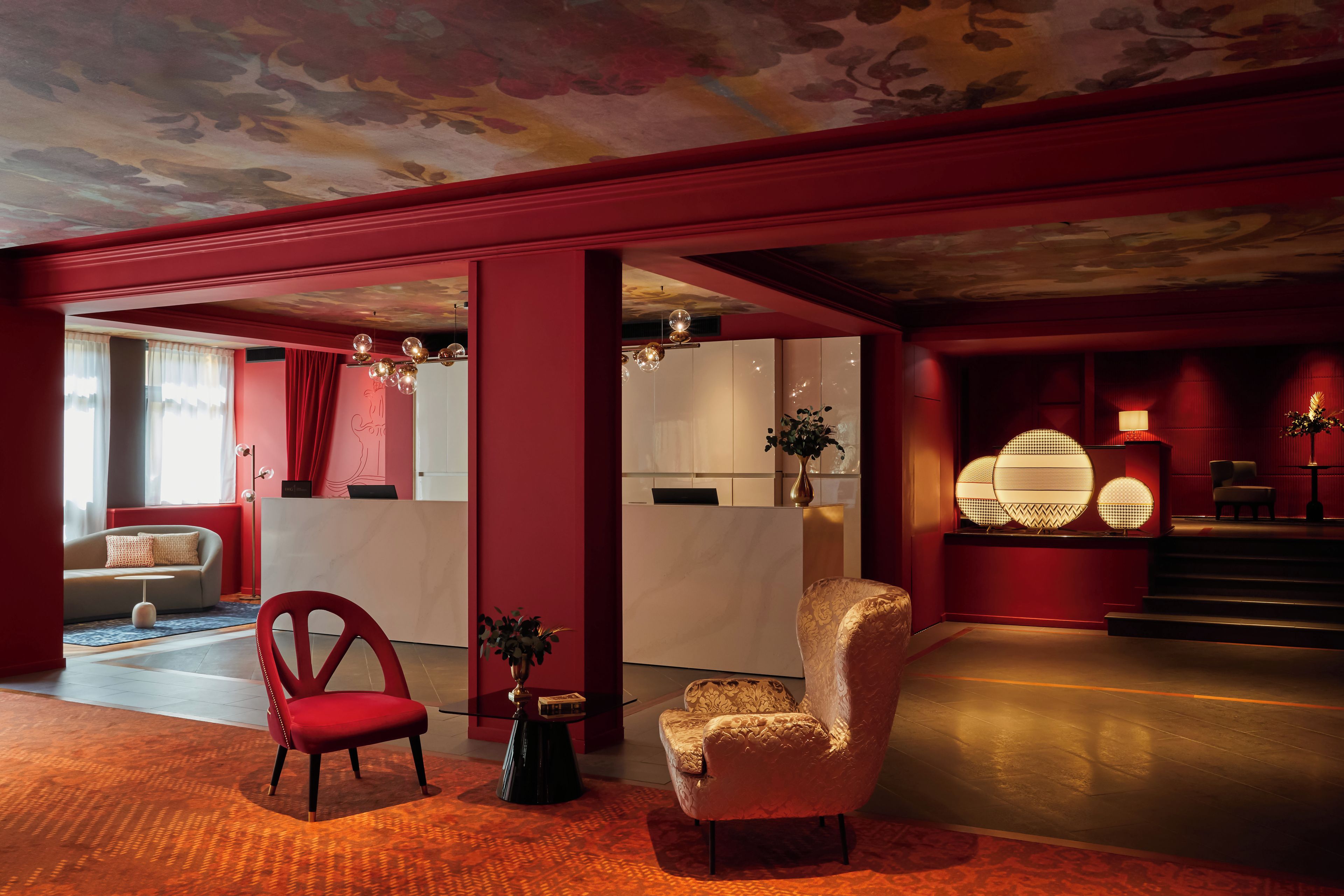 Un hall d’hôtel moderne aux couleurs rouge et blanc, avec un comptoir d’accueil, un espace salon et un escalier.