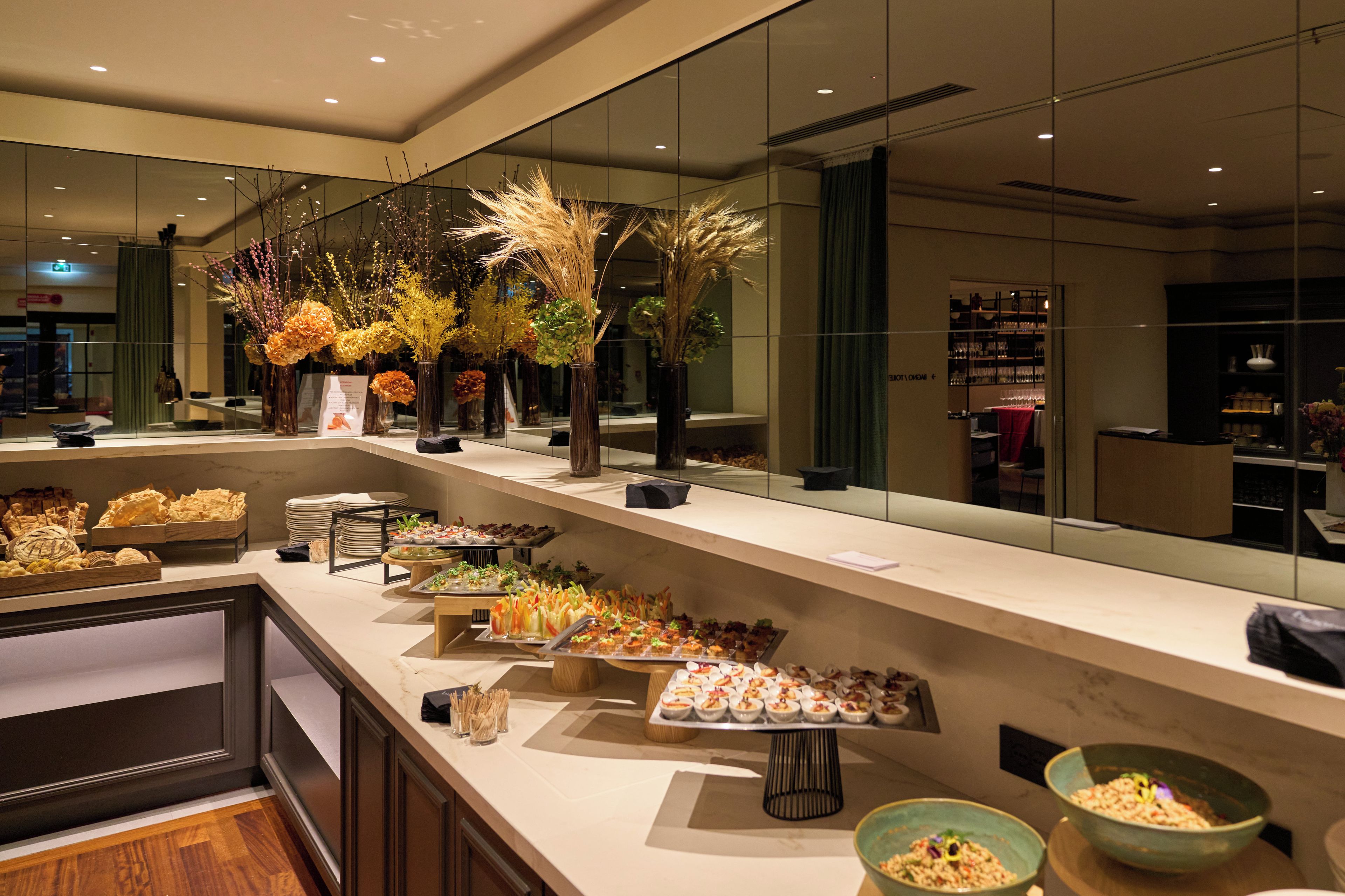 A buffet with various food items, a mirror reflecting the room, and decorative plants.