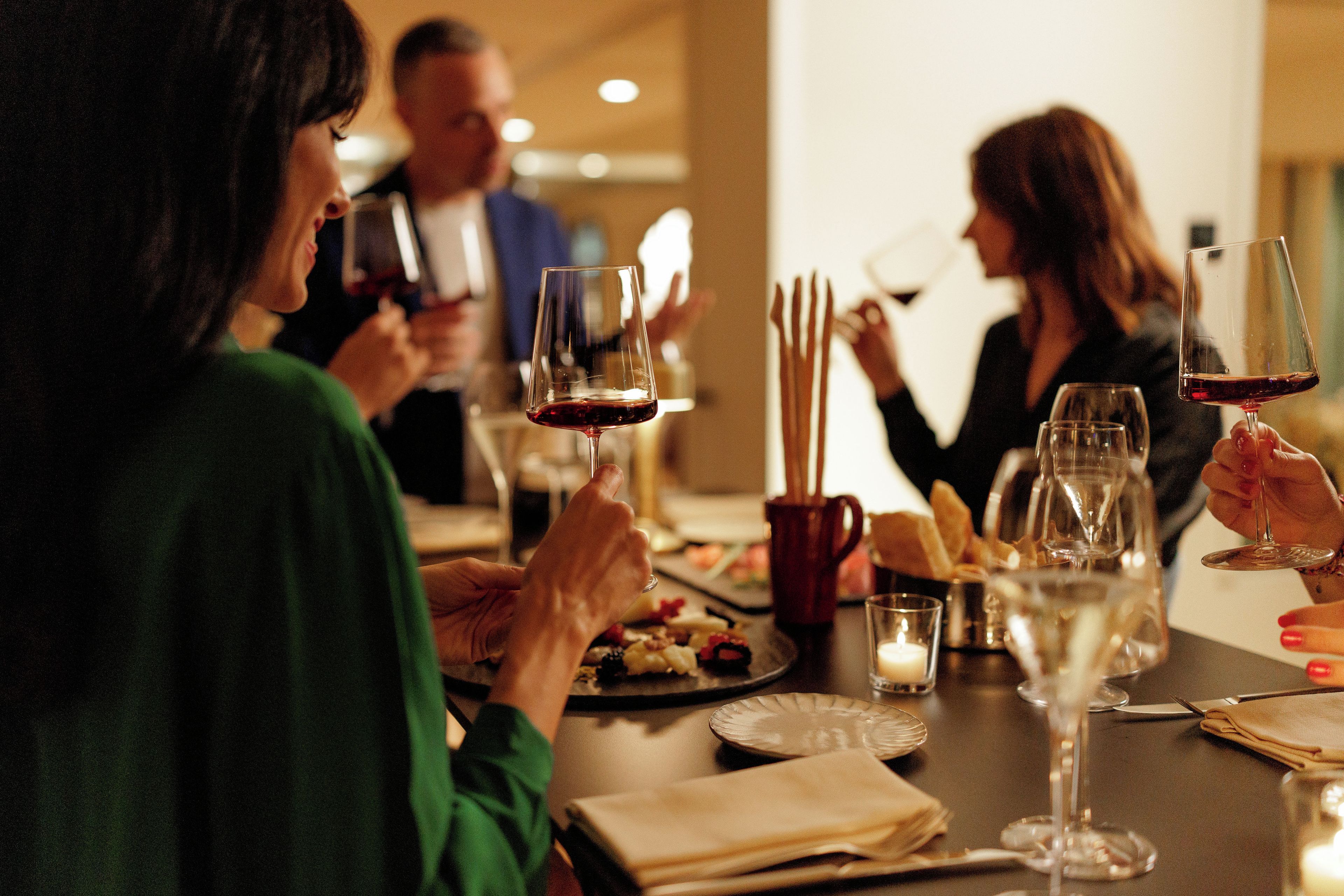 Un grupo de personas cenando en una mesa con copas de vino, platos de comida y una vela.