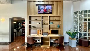 Una recepción con dos monitores de computadora, un televisor de pantalla plana montado arriba y una estantería de madera con objetos decorativos.
