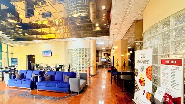Un vestíbulo de hotel con una recepción, zona de estar con sofás, un tablero de menú y una escalera que conduce a los pisos superiores.