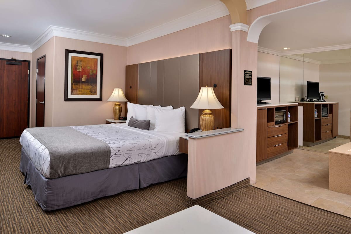 Habitación de hotel con una cama grande, dos lámparas de noche, un escritorio con una computadora y una kitchenette pequeña.