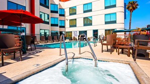 Un área de piscina de hotel con múltiples sillas de descanso, un jacuzzi y una piscina de color azul cristalino.
