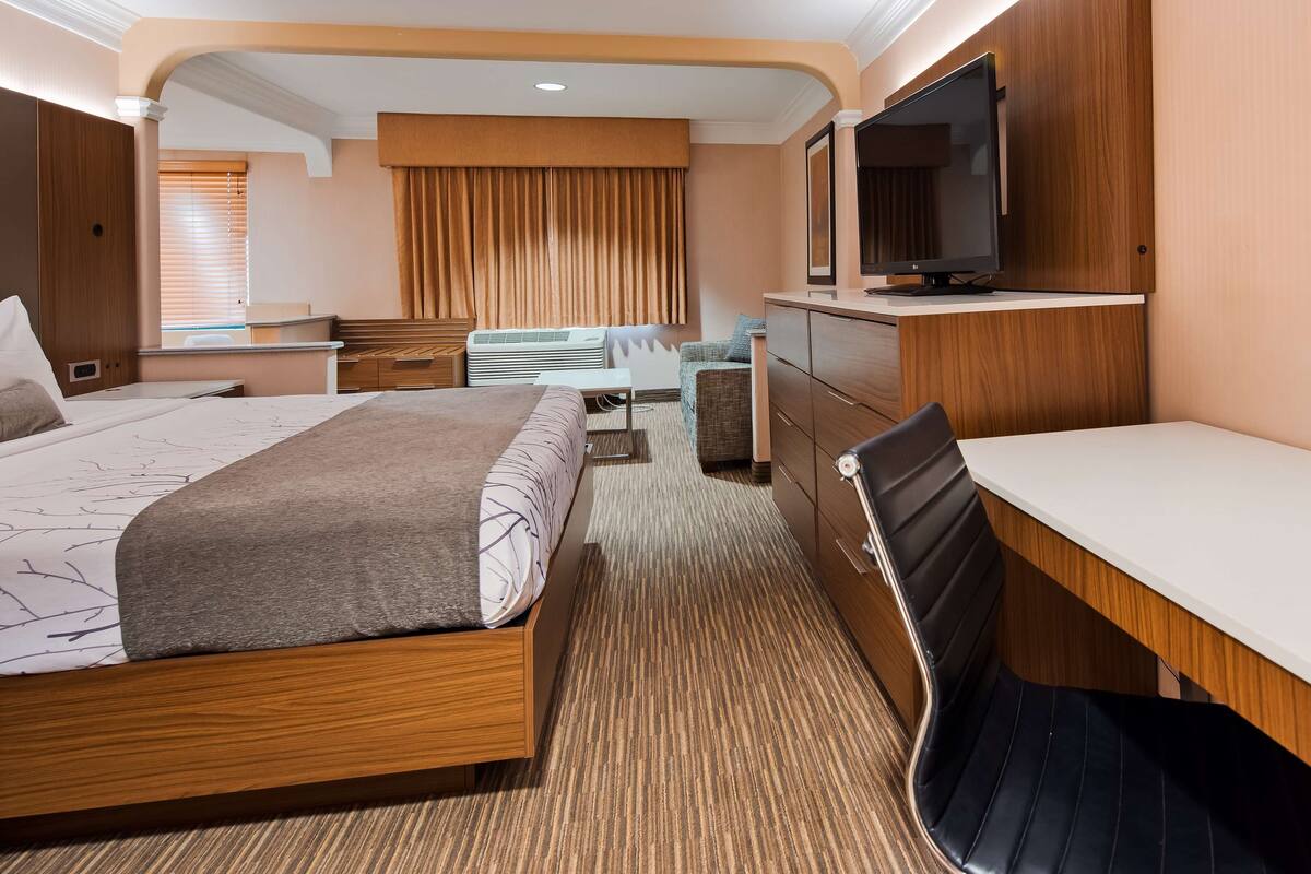 Una habitación de hotel con cama, escritorio, silla, televisión y minibar.