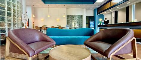 A lobby with a blue sofa, two leather armchairs, a round wooden coffee table, and a reception desk.