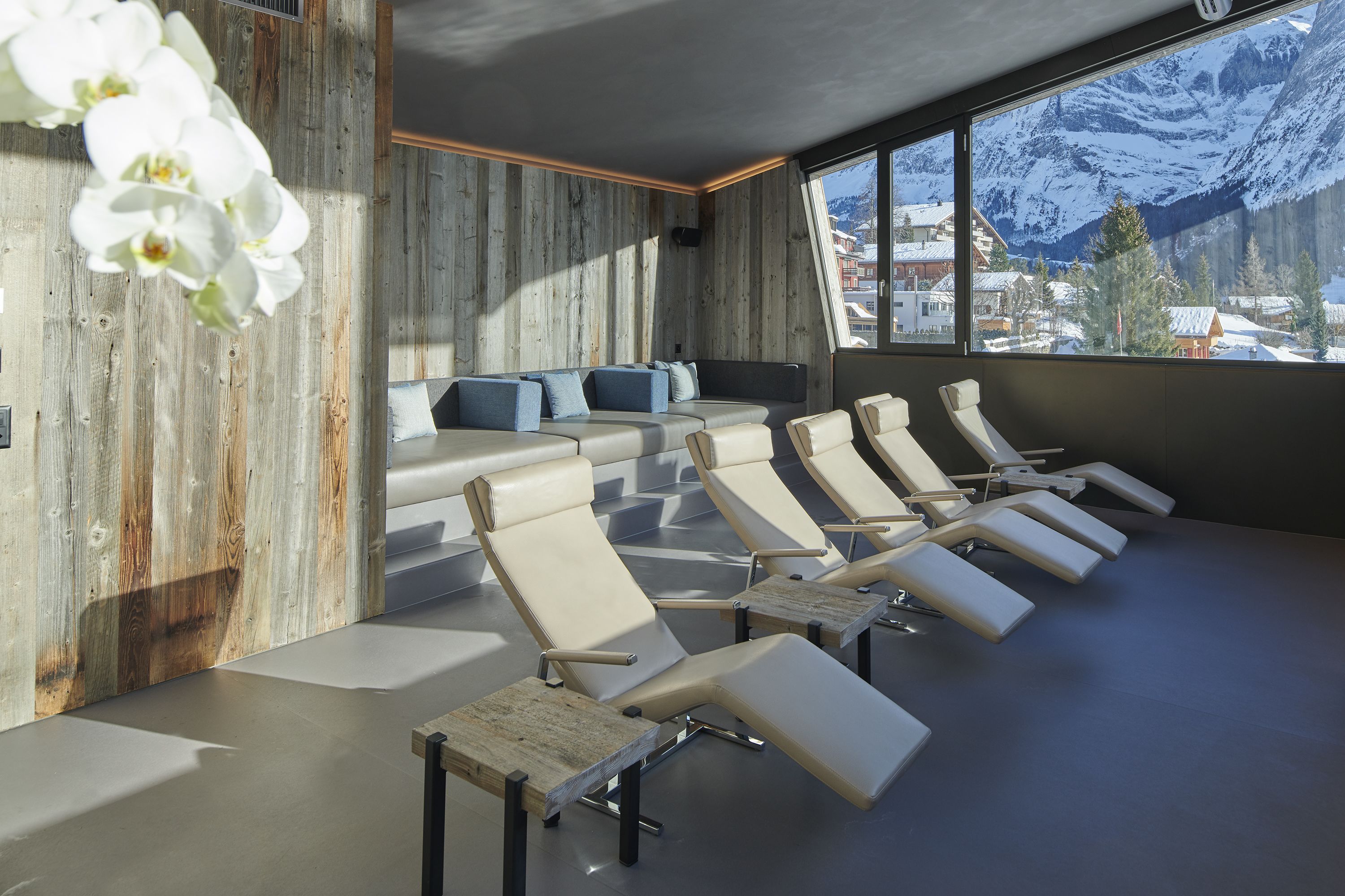A modern waiting area with a row of cushioned chairs, a wooden accent wall, and a large window offering a mountain view.