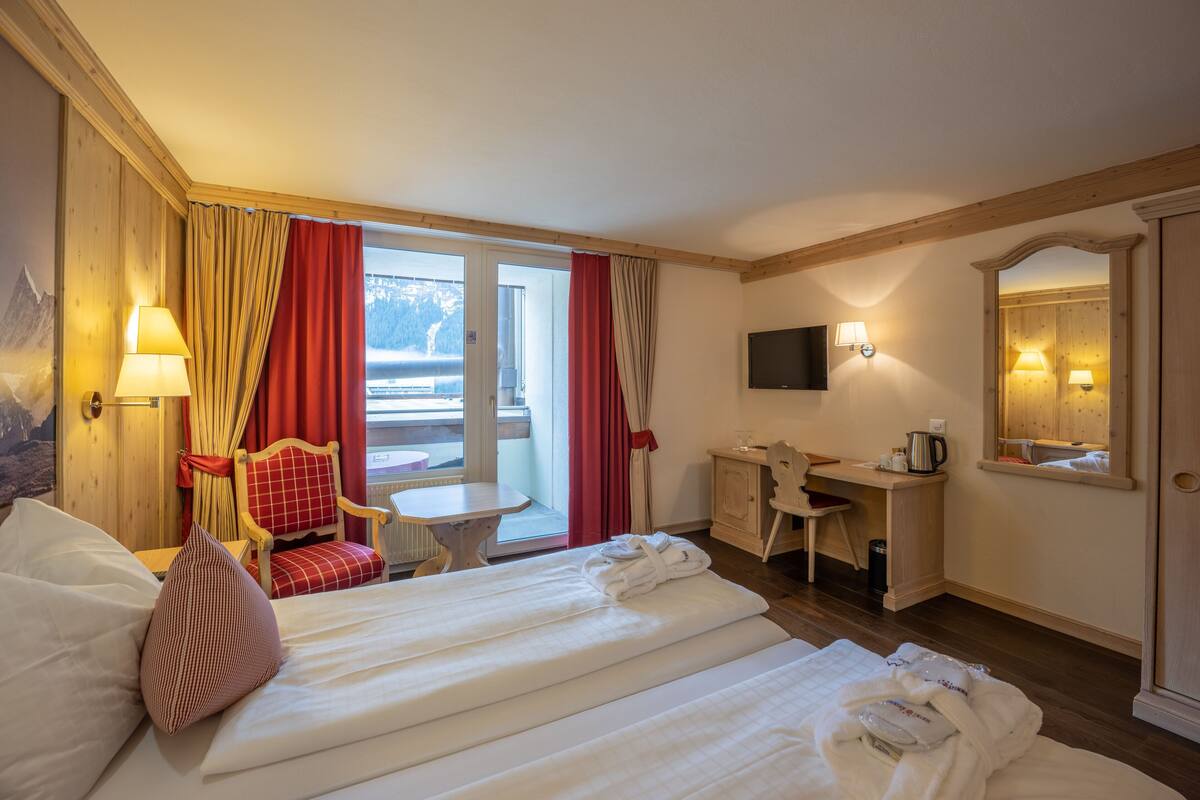 Una habitación de hotel con cama, escritorio, silla, mesa y ventana con cortinas.