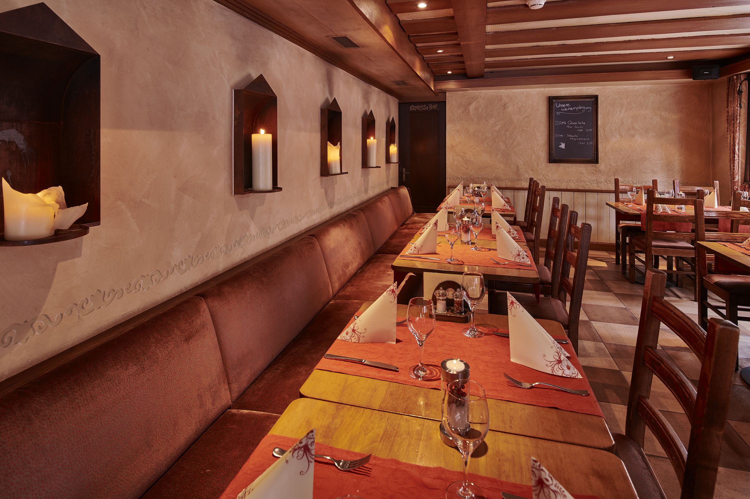 Un restaurante con mesas de madera largas, apliques de pared con velas y un menú en una pizarra.