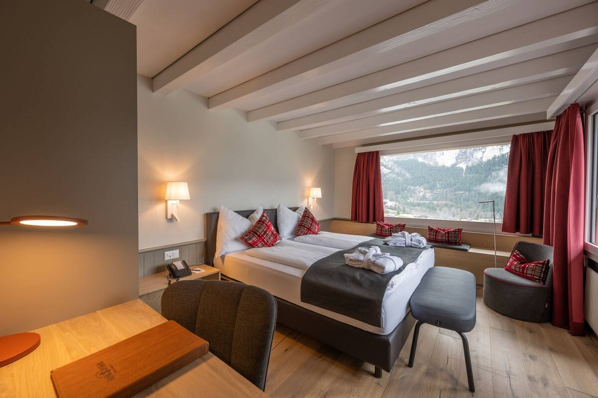Habitación de hotel con una cama grande, un escritorio, una silla y vistas al exterior.