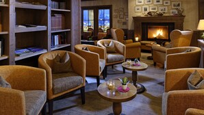 Un rincón acogedor con varios sillones, una chimenea y una estantería llena de libros.
