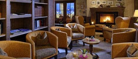 A cozy lounge area with multiple armchairs, a fireplace, and a bookshelf filled with books.