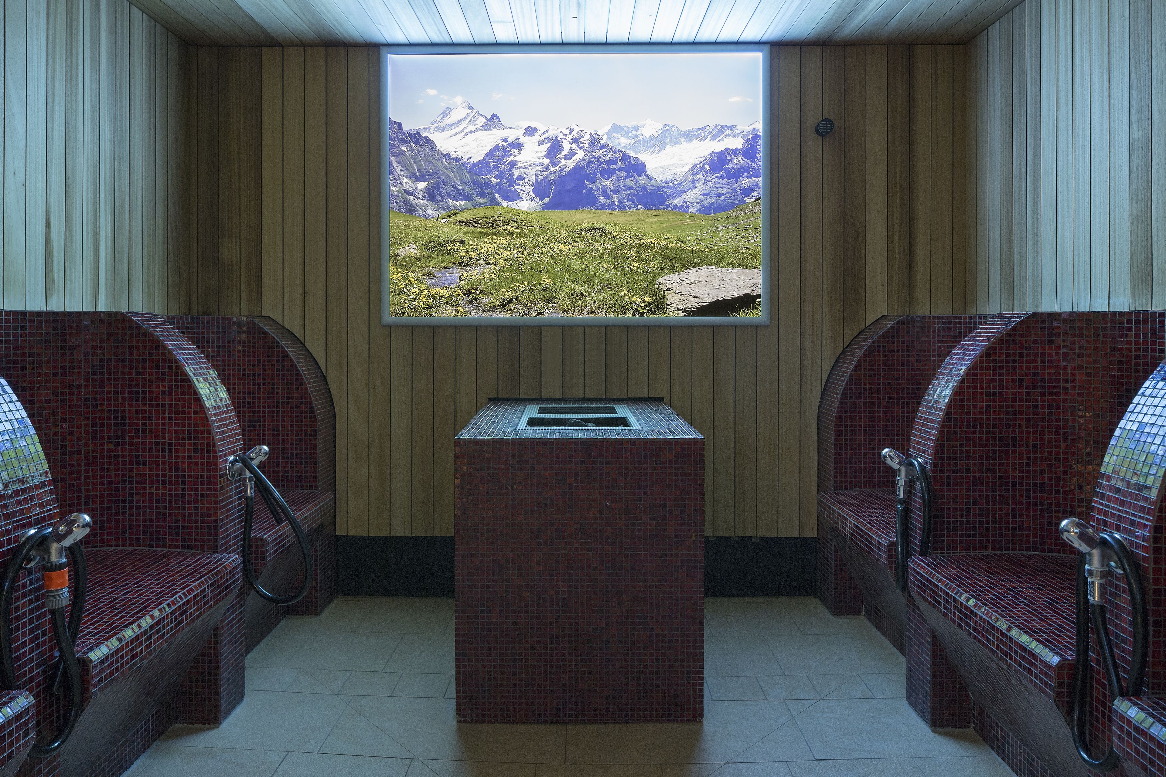 A sauna room with two red-tiled benches, a central table, and a large window offering a mountain view.