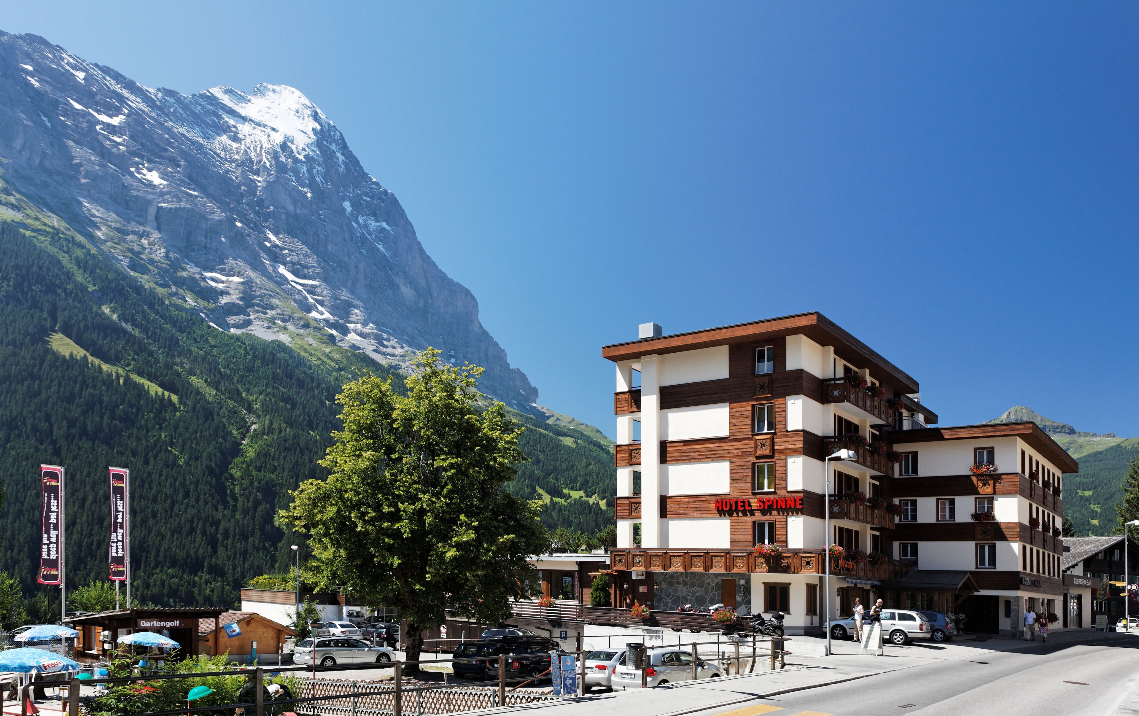 A hotel with a mountain backdrop, featuring a modern design with wooden accents and balconies with flower boxes.