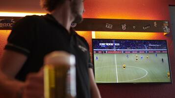 Iemand staat voor een televisiescherm waarop een voetbalwedstrijd wordt vertoond.