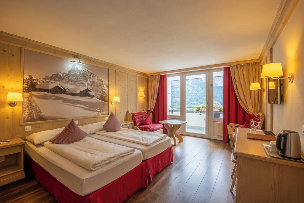 Habitación de hotel con dos camas, un escritorio, una silla, una mesa y un ventanal grande con cortinas.