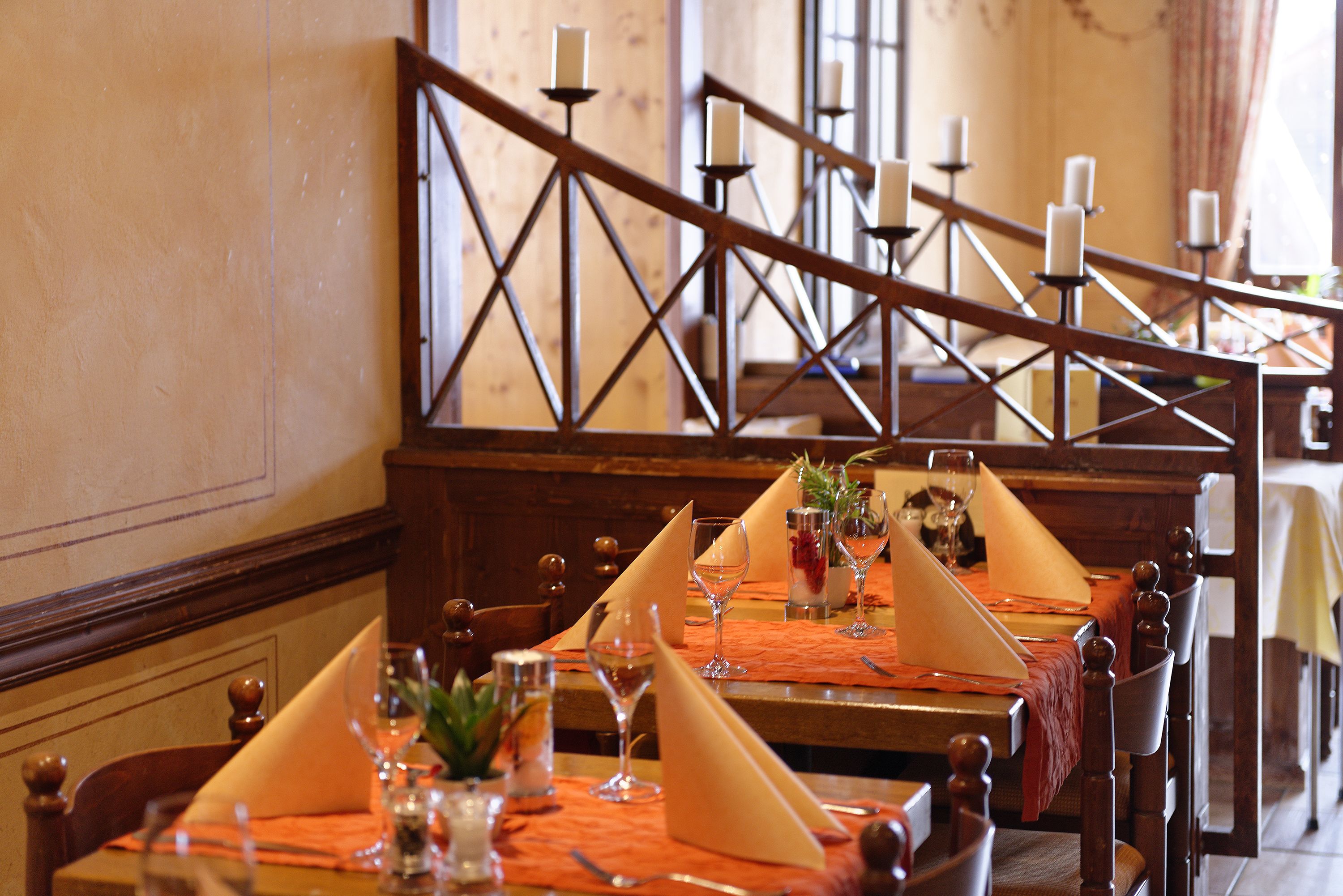 A dining area with wooden tables, orange placemats, and candles on a wooden railing.