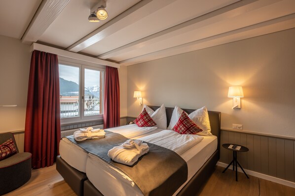 A hotel room with a large bed, two bedside lamps, a small table, and a view of the outdoors.