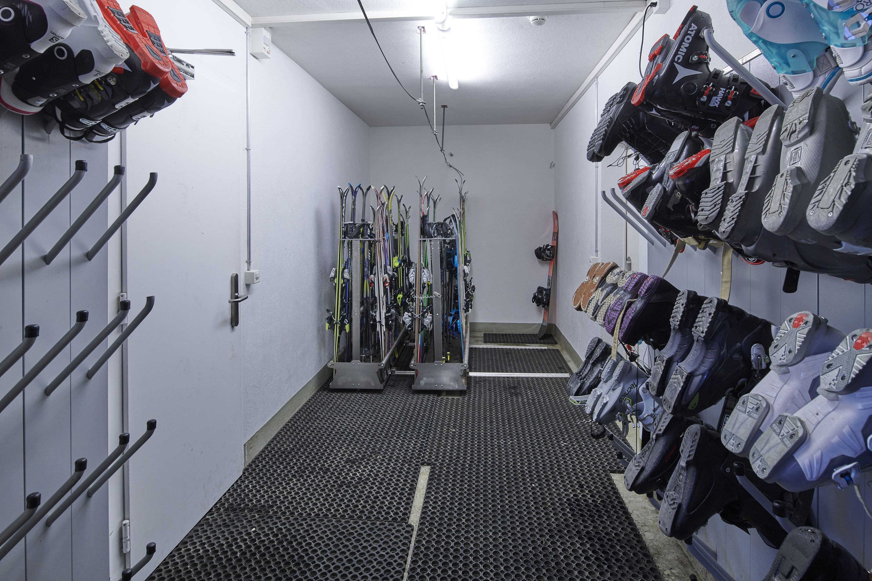 A ski storage room with racks for skis and boots, a central ski lift, and a textured floor.