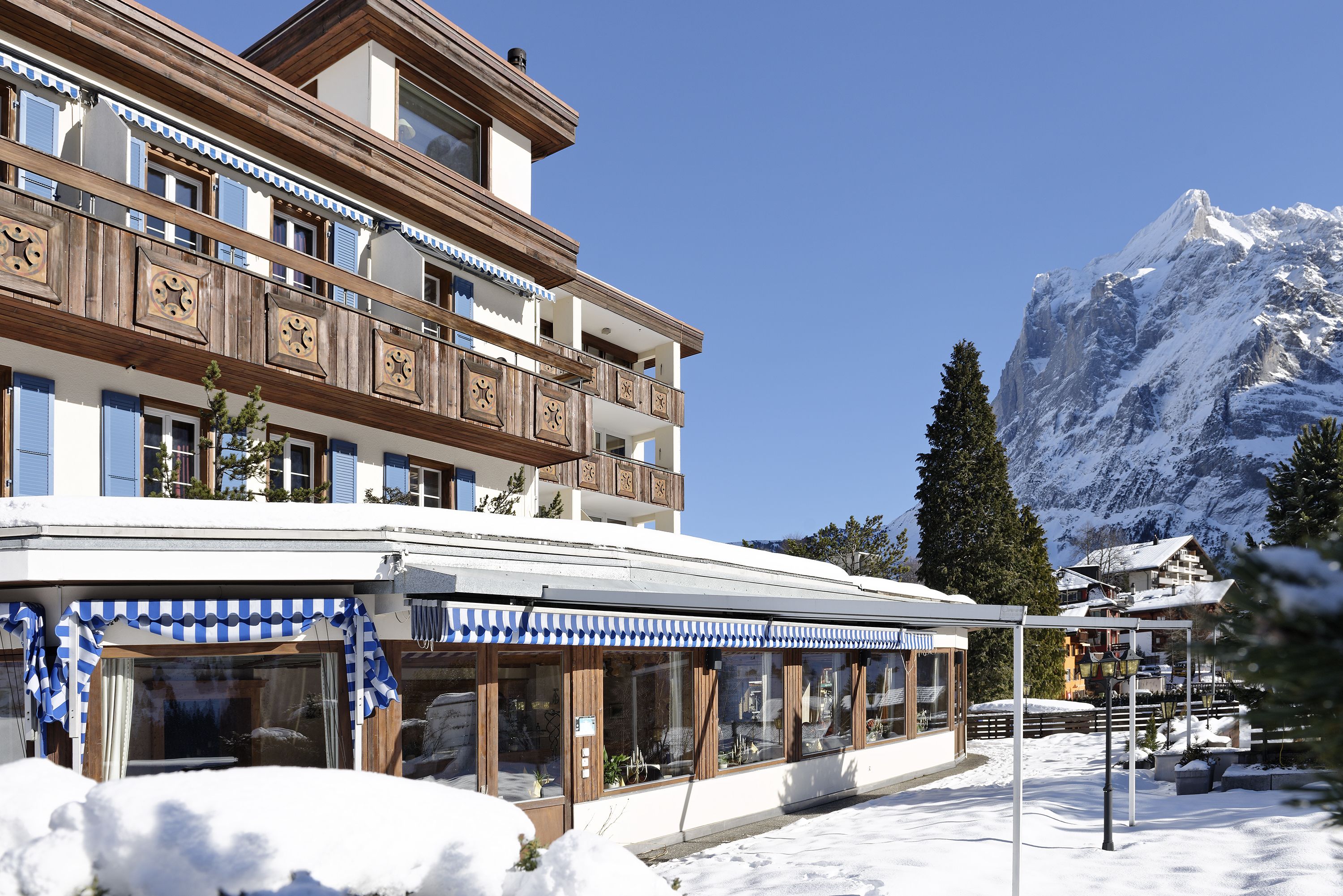 A multi-story hotel with wooden balconies and large windows, set against a snowy mountain backdrop.