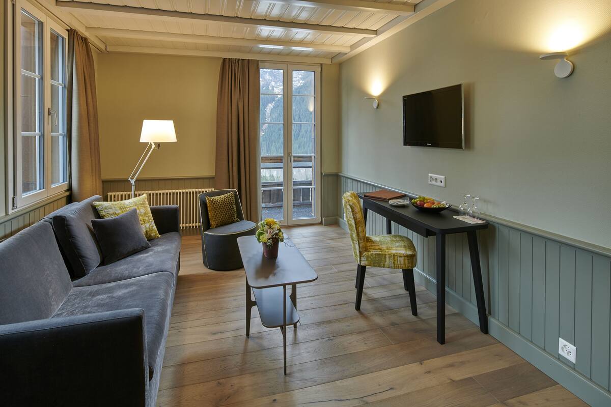 Una sala de estar acogedora con un sofá, una mesa con un florero, una silla y un televisor montado en la pared.