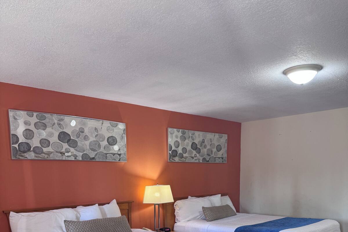A hotel room with two beds, a nightstand, a lamp, and a chair.