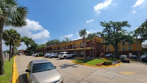 A parking lot with several cars, a building with multiple balconies, and a clear blue sky. - Twin Star Lodge (Biloxi)