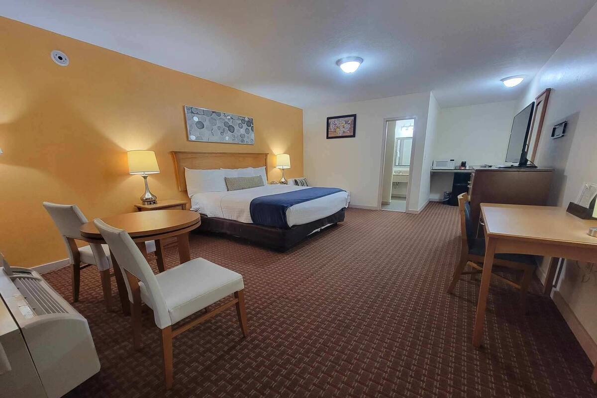A hotel room with a bed, a desk, a chair, a small table, and a bathroom visible through an open door.