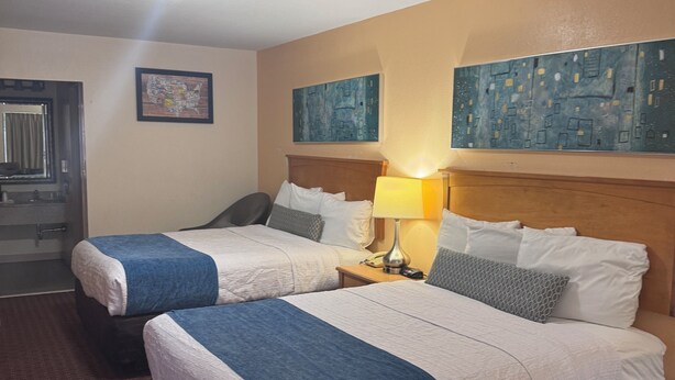 A hotel room with two beds, a nightstand with a lamp, a wooden headboard, and artwork on the walls. - Twin Star Lodge (Biloxi)