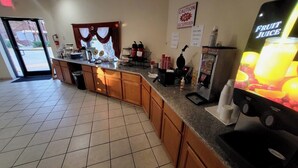 A kitchen area with a fruit juice dispenser, a caution sign, and a window with curtains. - Twin Star Lodge (Biloxi)
