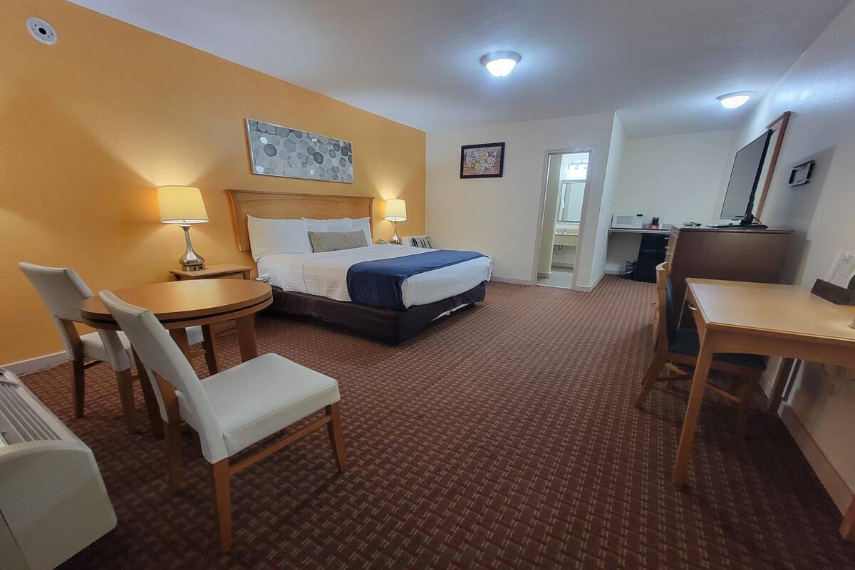 A hotel room with a bed, a desk, a chair, a lamp, and a small table.