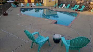 A swimming pool with turquoise chairs and a fire pit.