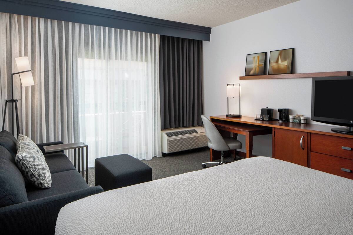 A hotel room with a bed, a desk, a chair, a TV, and a coffee maker.