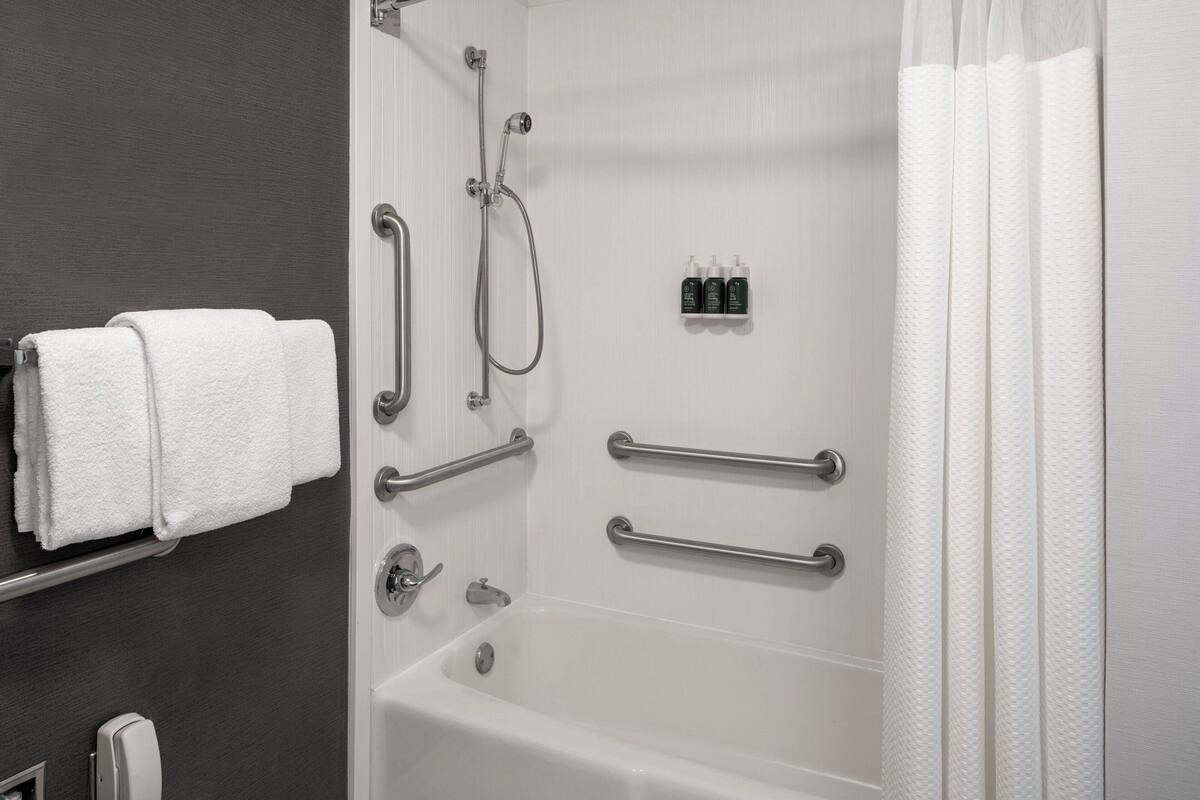 A bathroom with a bathtub, handrails, a towel rack, and a shower control panel.