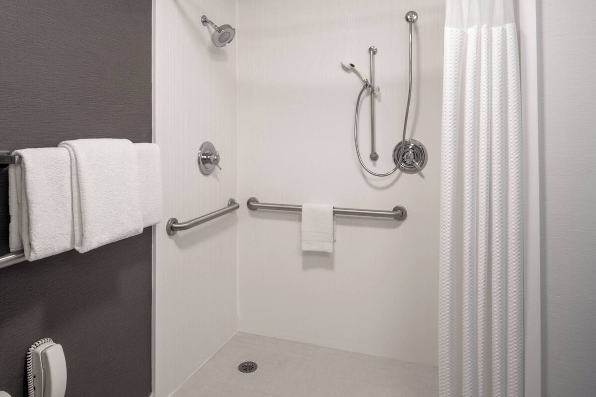 A shower area with a grab bar, a towel rack, and a showerhead.