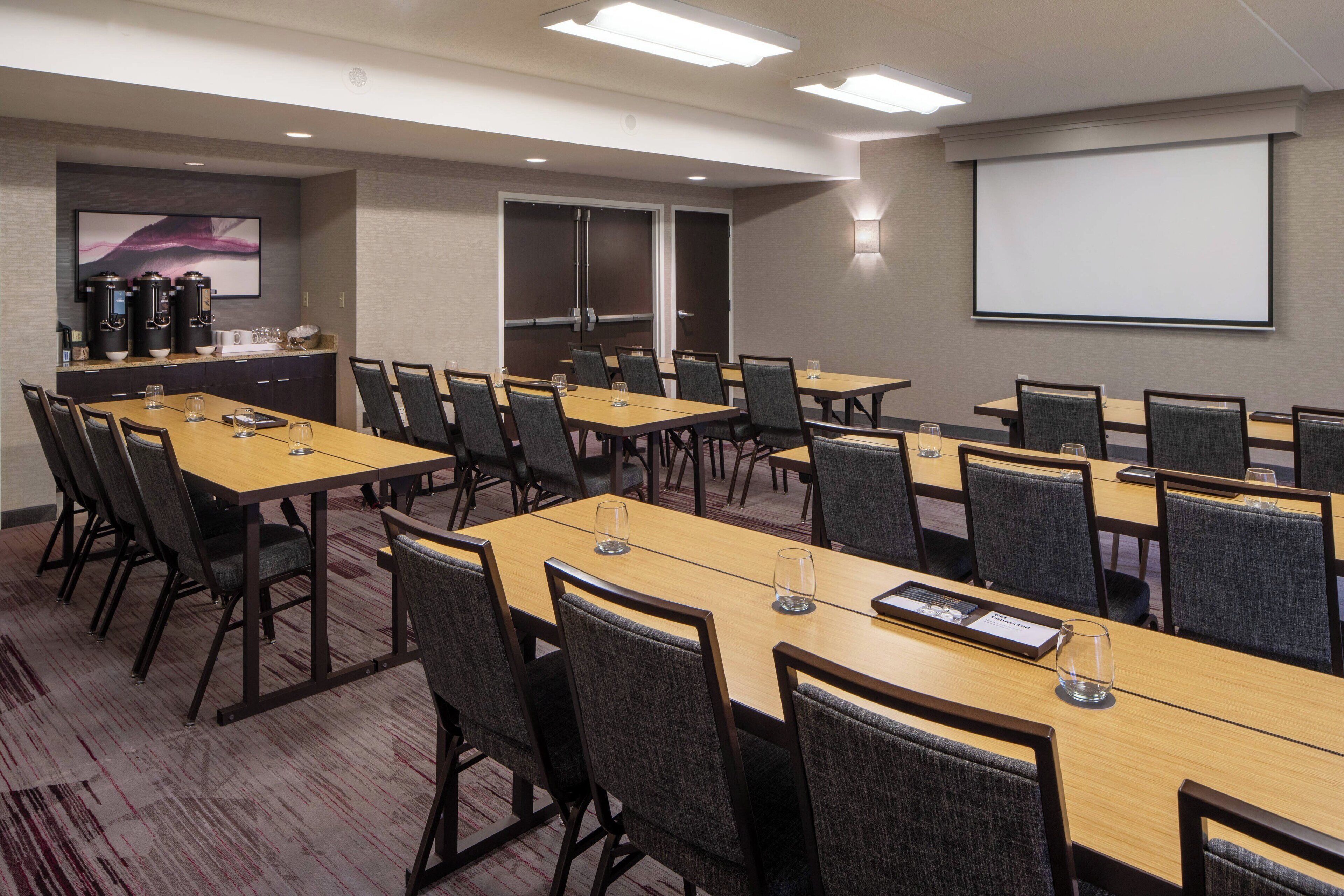 Una sala de conferencias con varias mesas y sillas, una pantalla de proyector y una estación de café.