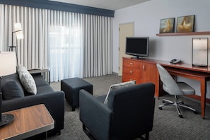 Una habitación de hotel con sofá, reposapiés, escritorio, silla, televisor y lámpara.