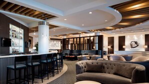 A modern bar area with a counter, bar stools, and seating arrangements including sofas and a round table. - Sheraton Cavalier Calgary Hotel (Calgary)
