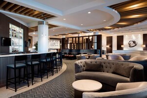 A modern bar area with a counter, bar stools, and seating arrangements including sofas and a round table.