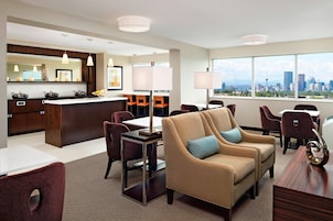 A modern hotel room with a city view, a dining area, and a kitchen.