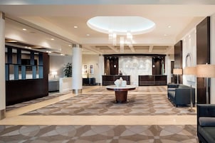 A modern lobby with a central round table, seating areas, and a reception desk.