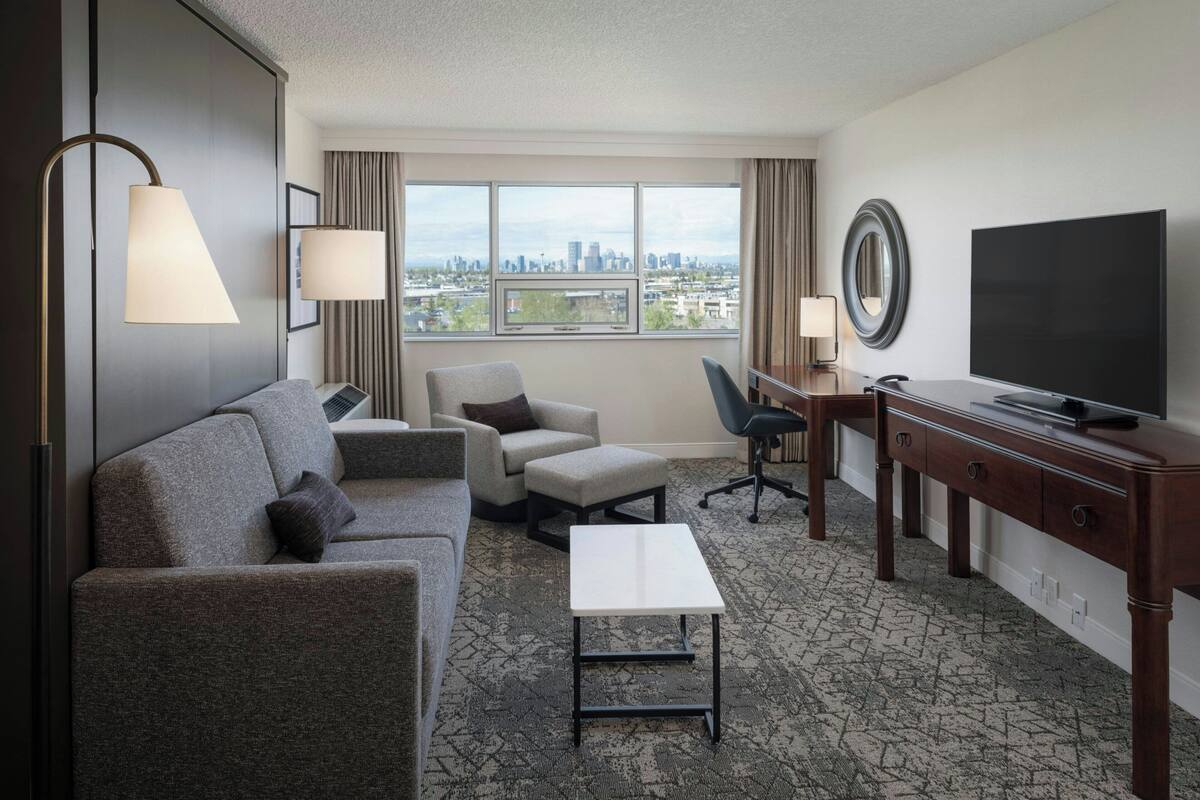 A hotel room with a sofa, armchair, desk, and TV.