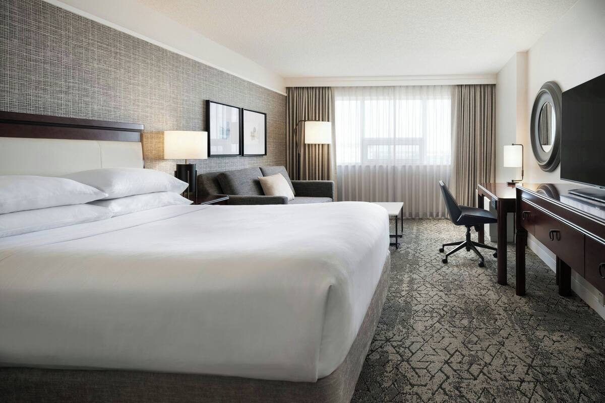 A hotel room with a large bed, a desk with a chair, a television, and a window with curtains.