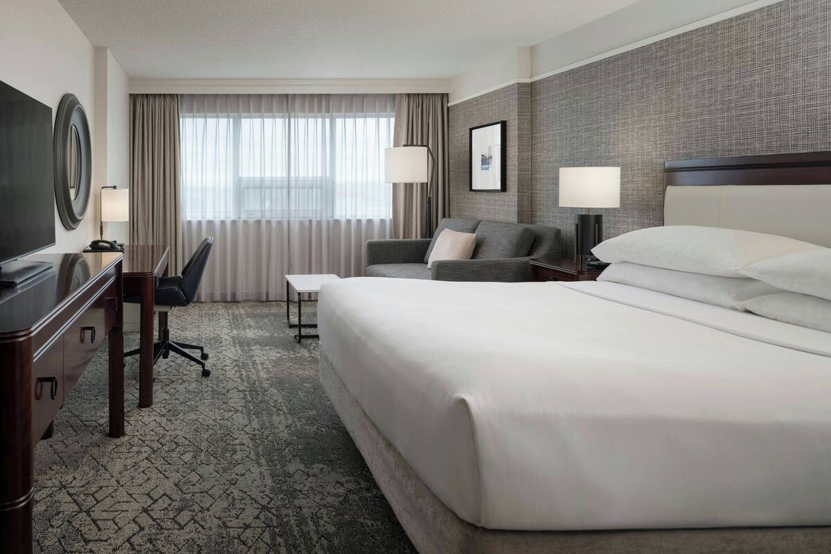 A hotel room with a large bed, a desk with a chair, a television, and a window with curtains.