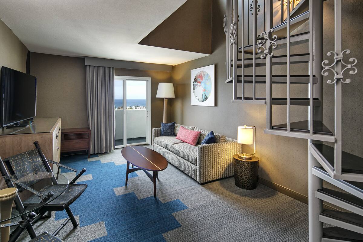A hotel room with a sofa, a TV, a lamp, and a view of the city.