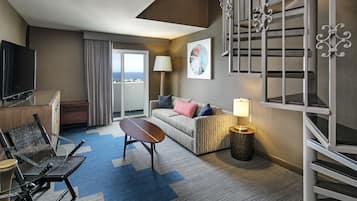 A hotel room with a sofa, a TV, a lamp, and a view of the city.