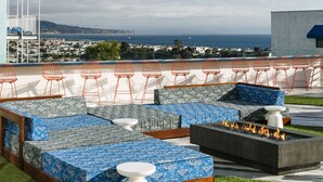 An outdoor seating area with blue patterned cushions, orange wire chairs, and a fire feature. - Hotel Hermosa (Hermosa Beach)