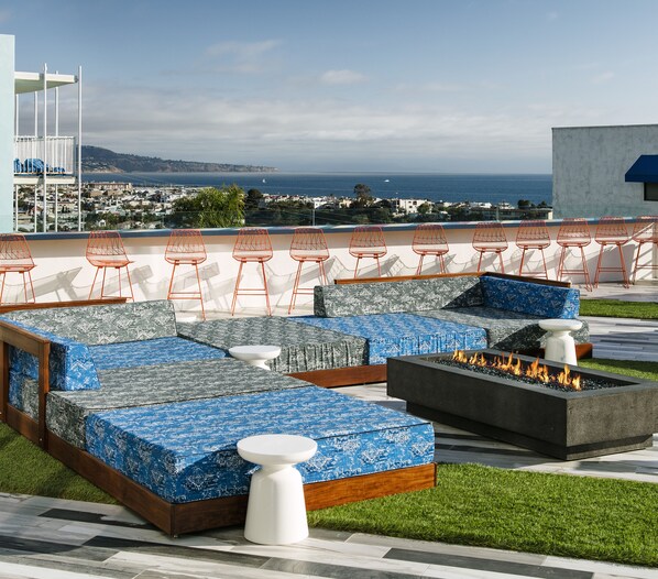 An outdoor seating area with blue patterned cushions, orange wire chairs, and a fire feature. - Hotel Hermosa (Hermosa Beach)