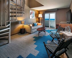 A hotel room with a sofa, a coffee table, a dining table with chairs, a TV, and a balcony with a view.