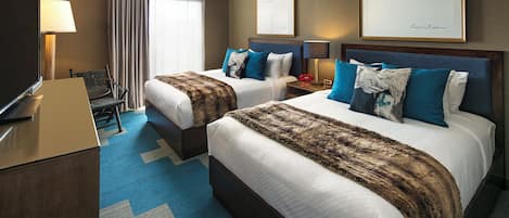 A hotel room with two beds, a desk, a TV, and a large window with curtains.
