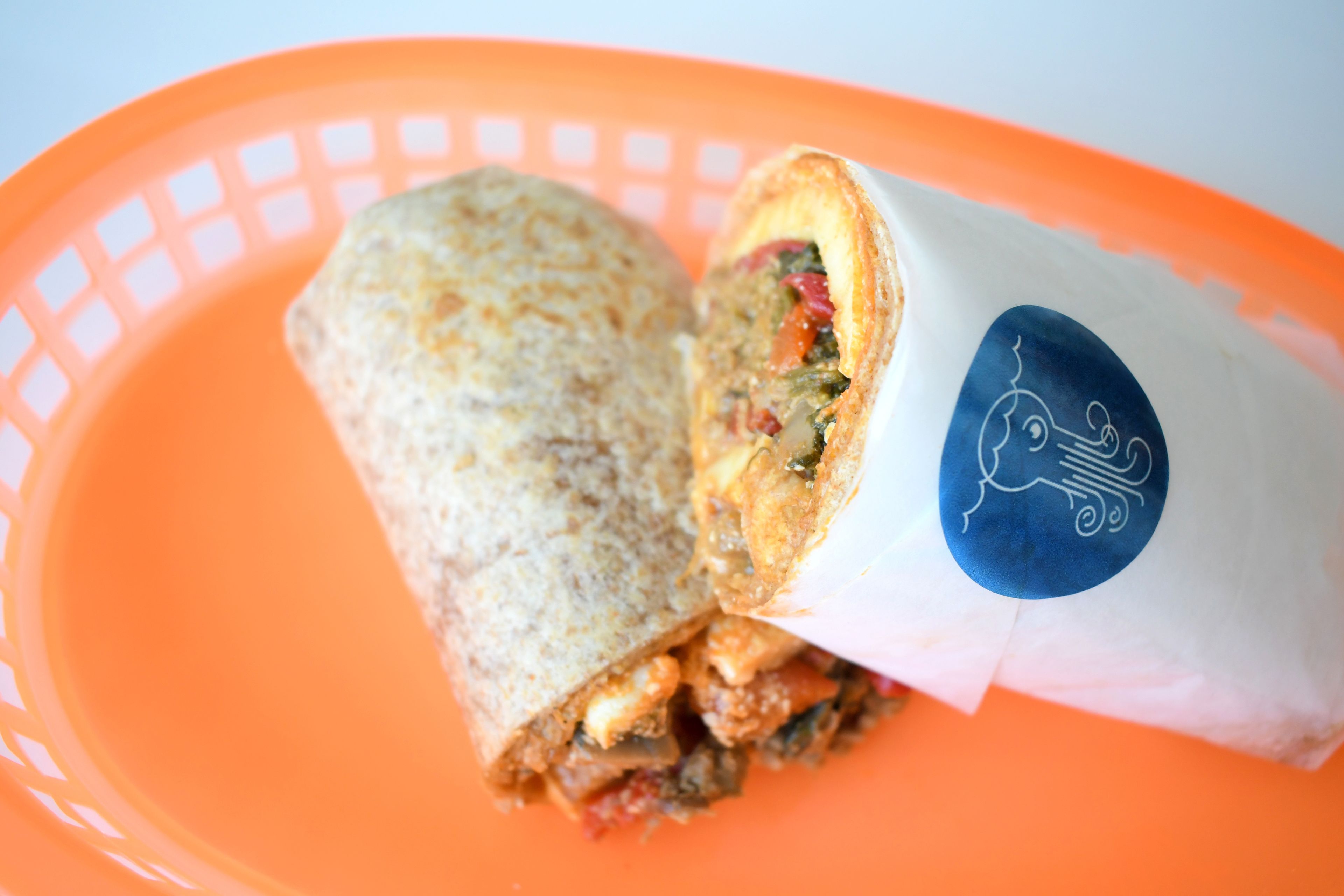 A burrito in a paper wrapper on an orange plate.